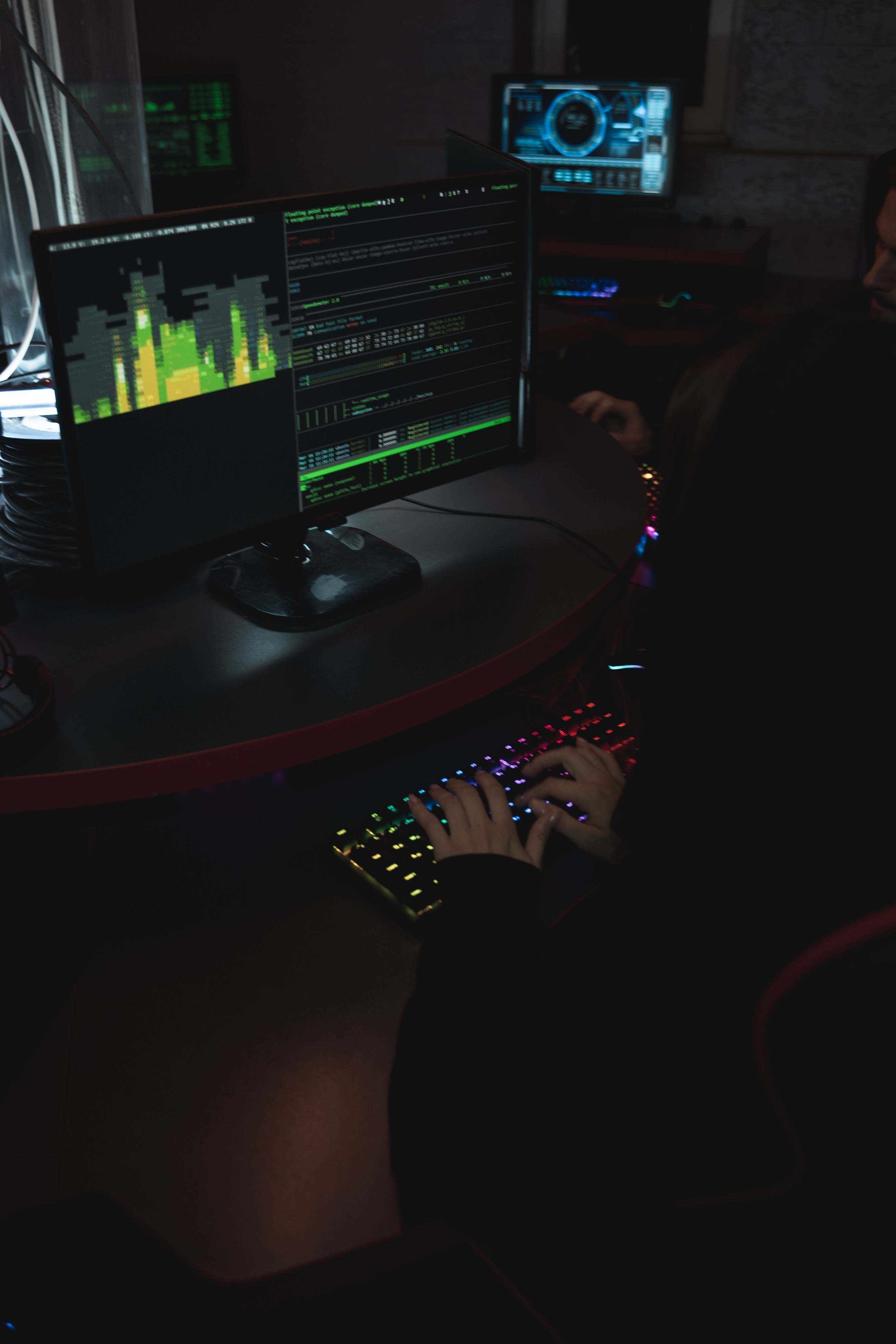 Hands typing on a keyboard in a dark room with coding screens